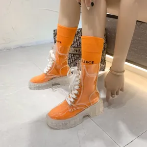 Detail view of clear PVC lace-up boots paired with bright orange crew socks on model