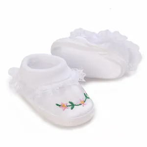 Close-up of white princess baby shoes with delicate floral embroidery and lace trim.