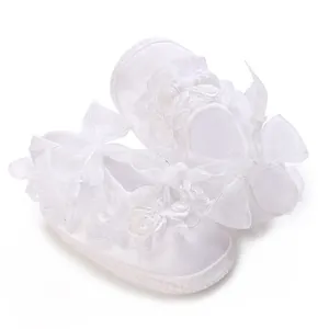 Close-up of white lace baby princess shoes with ribbon bow and flower detail for girls