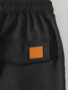 Detalle de pantalones cargo negros con cintura elástica y bolsillo con parche naranja