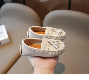 Gros plan de mocassins beiges pour bambins avec glands, texture croco et coutures main