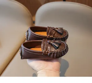 Vue détaillée de mocassins marron foncé pour enfants avec pompons élégants et texture en cuir