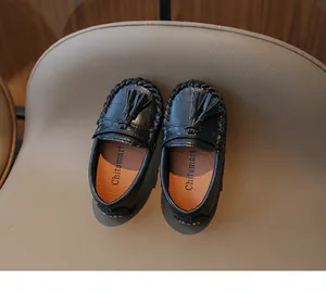 Vue détaillée de mocassins noirs à glands pour enfants sur un siège beige de style anglais.