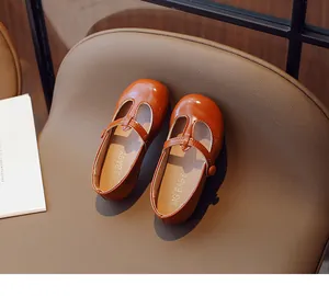 Vintage brown T-strap leather shoes for toddler girls displayed on a leather chair.