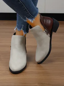 Detailweergave tweekleurige damesenkellaarzen met puntige neus en zijrits op houten vloer.