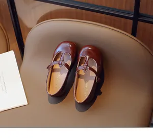 Classic dark brown T-strap leather shoes for toddler girls on a leather background