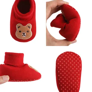 Close-up view of soft red baby sock shoe showing flexible sole and anti-slip dotted bottom.