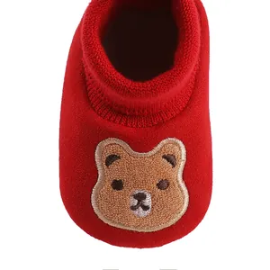 Close-up macro detail of a soft red baby sock shoe featuring a cute cartoon bear embroidery