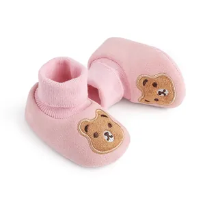 Close-up of pink soft-soled baby booties with a cute cartoon bear embroidery patch.
