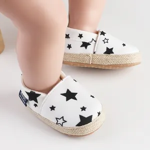 Primer plano de zapatos blancos para bebés con estrellas negras y suelas envueltas en yute.