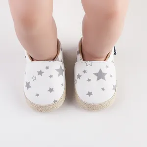 Primer plano de zapatos blancos para bebés con patrón de estrellas grises y suela de yute.