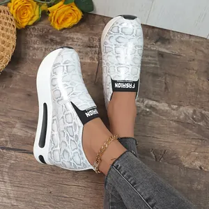 Dettaglio di sneaker slip-on con stampa serpente e suola alta su sfondo di legno