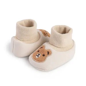 Close-up of soft-soled beige baby booties with a cute embroidered cartoon bear detail