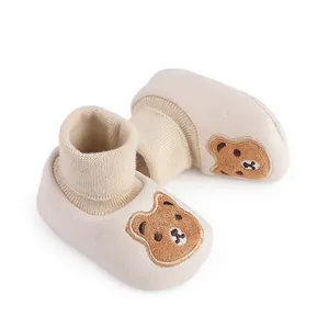 Close-up of soft cream-colored baby booties with embroidered bear face and knitted cuffs