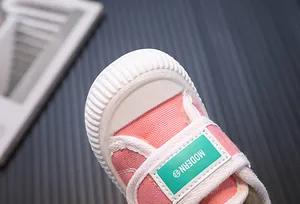 Close-up of a pink children's canvas shoe showing the white toe cap and green label