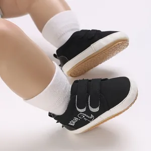 Nahaufnahme schwarzer Babylauflernschuhe mit Dinosaurier-Stickerei und Klettverschluss