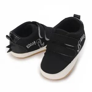 Detail von schwarzen Baby-Lauflernschuhen mit Dino-Stickerei und Klettverschluss
