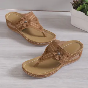 Detail von braunen Keil-Flip-Flops für Damen mit Blumendeko und Lochmuster am Riemen.