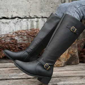 Détail de bottes cavalières noires à bout pointu, talon épais et boucle dorée
