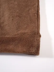Detailopname van bruine koraalfleece stof met zachte pluizige textuur en afgewerkte zoomrand