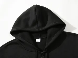 Détail d'un sweat à capuche noir avec fermeture éclair montrant la capuche et l'étiquette.