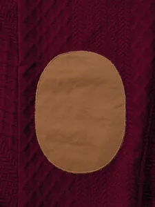 Vista detallada del tejido jacquard burdeos y el parche ovalado marrón para sudadera de hombre
