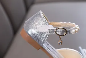 Detailaufnahme von silbernen Glitzer-Prinzessinenschuhen mit Perlenriemen und Anhänger.