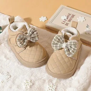 Close-up of beige quilted baby winter boots with large plaid bow and warm fleece lining