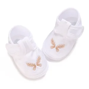 Detailed macro view of white baby christening shoes with golden butterfly embroidery detail.