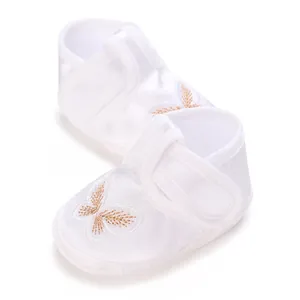 Detailed macro view of white satin baby girl shoes with golden butterfly embroidery