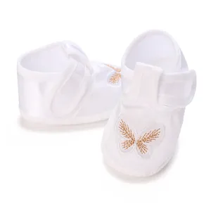 Close-up of elegant golden butterfly embroidery on white soft-sole baptism baby shoes