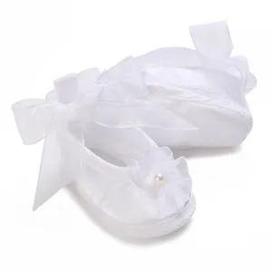 Detail view of white satin baby christening shoes with pearl flower and ribbon bow