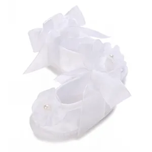Close-up of white baby baptism shoes with large organza bow and pearl flower detail