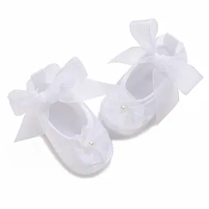 Detailed view of baby christening shoes with white ribbon bows and pearl flowers
