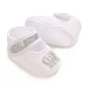 Close-up detail of white baby girl baptism shoes featuring a silver glitter crown design