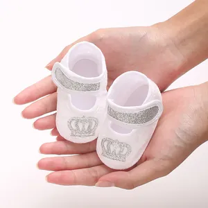 Close-up detail of white baby baptism shoes featuring a silver glitter crown and strap