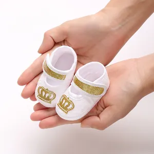 Close-up detail of white lace baby girl baptism shoes with gold glitter crown emblem