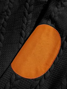 Detailed macro view of an orange elbow patch on a black textured jacquard Henley shirt
