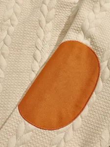 Macro detail of heavyweight jacquard knit fabric featuring a contrast orange elbow patch
