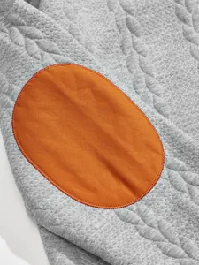 Close-up detail of men's quilted grey sweatshirt featuring a vibrant orange oval elbow patch