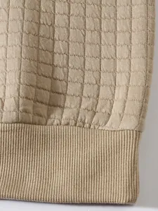 Nahaufnahme eines beigen Herren-Sweatshirts mit quadratischer Steppung und Rippbündchen.