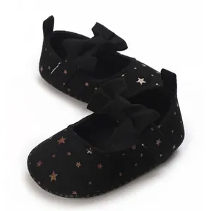 Primer plano de elegantes zapatos negros para bebé con estrellas doradas y lazos clásicos.