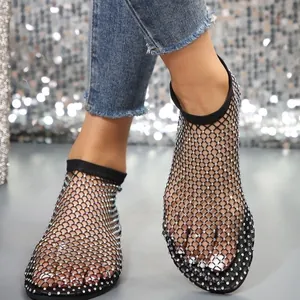 Close-up of black fishnet flat sandals with sparkling rhinestones on model's feet.