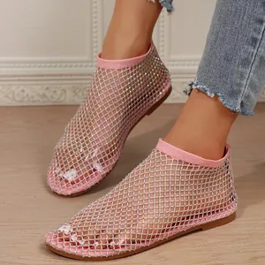 Close-up view of pink rhinestone-studded mesh flat sandals for women on a wooden floor