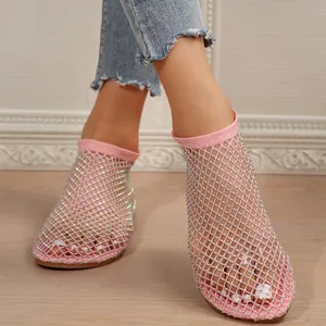 Close-up view of pink flat sandals featuring rhinestone mesh upper worn with blue denim jeans