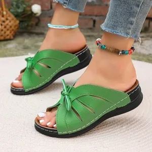 Nahaufnahme von grünen Peep-Toe-Hausschuhen mit Hohlmuster und süßer Schleife und Sohle