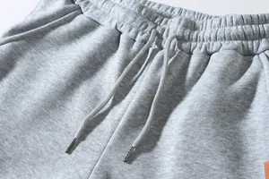 Close-up detail of grey sweatpants showing elastic waistband and drawstring with metal tips.