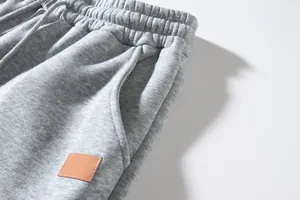 Close-up detail of grey sweatpants showing elastic waistband and leather patch texture