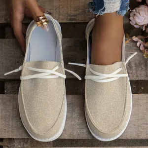 Close-up of women's beige canvas loafers with decorative white laces and rustic background