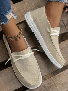 Detailed view of beige glitter canvas loafers with thick white soles on wooden planks.